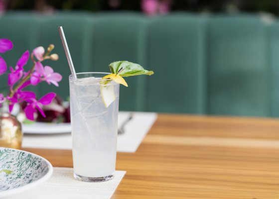 A summer cocktail, garnished with basil, on a wood table. 